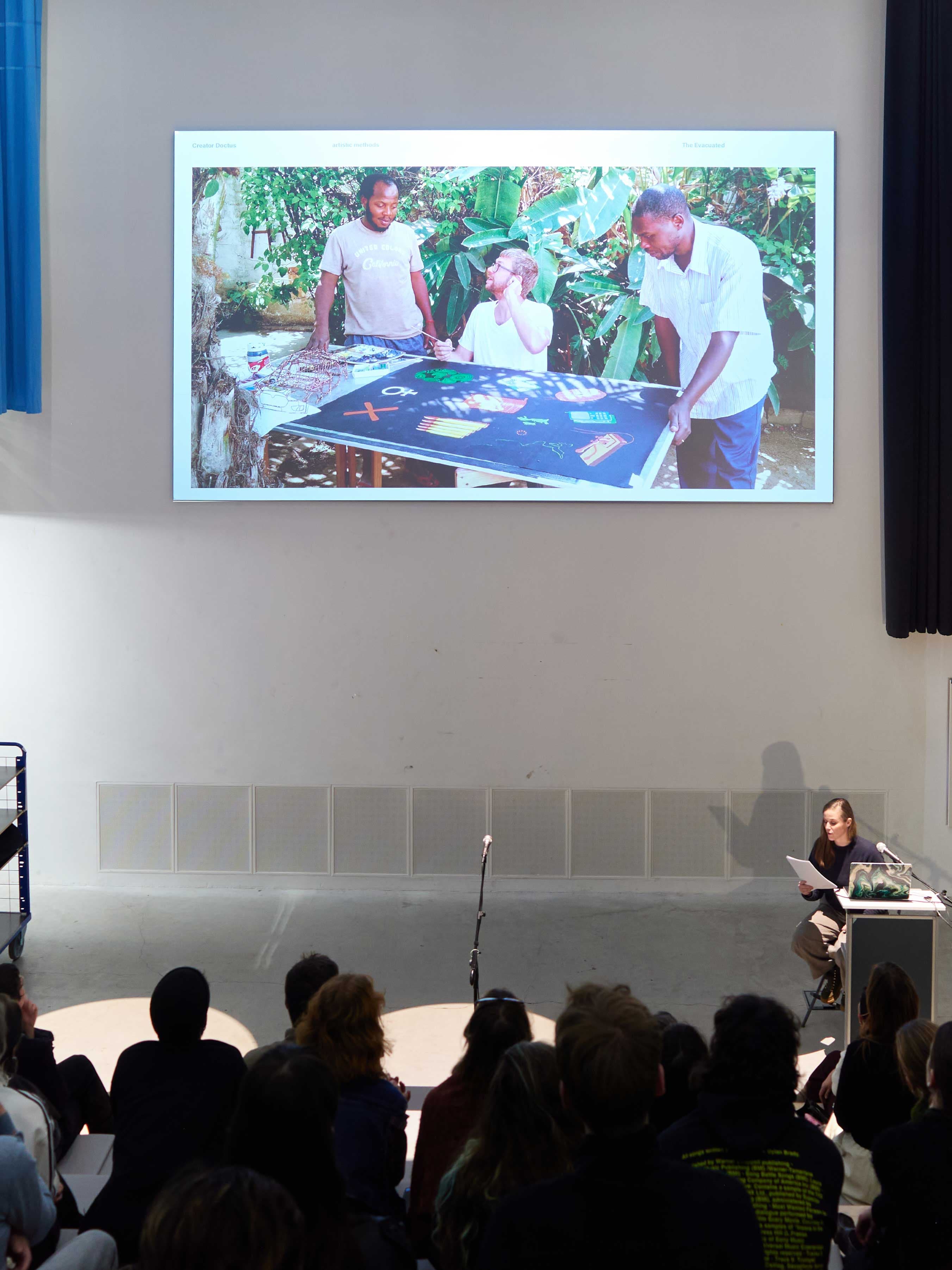 The image shows an event with an image projected overhead, and the audience in the foreground.