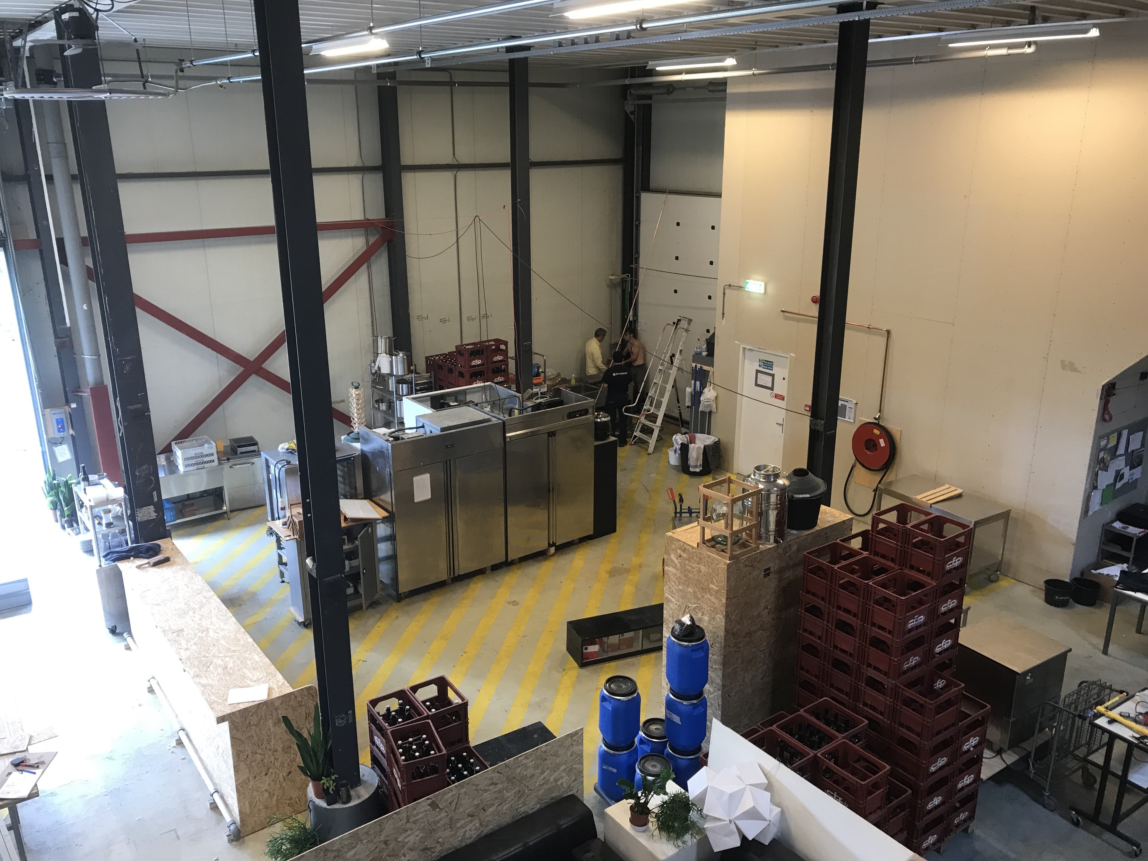 The image shows a warehouse space filled with kegs and appliances for brewing beer.